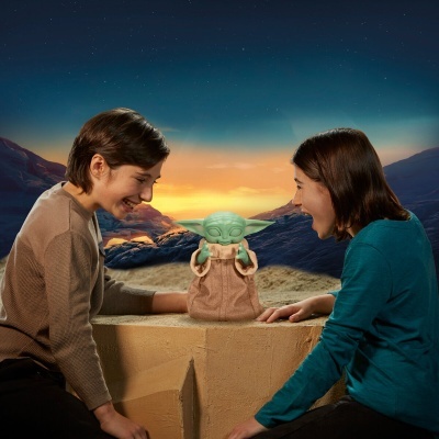 Figura de ação Baby Yoda entre duas crianças num cenário de montanhas e pôr do sol