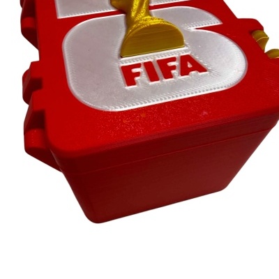 Caixa vermelha com tampa branca e vermelha, texto FIFA e figura dourada tipo troféu