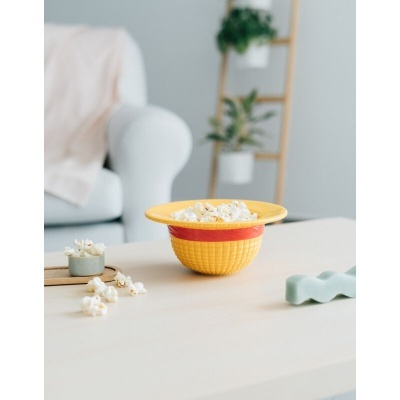 Três bowls coloridos com pipocas numa mesa branca, cadeira e plantas ao fundo