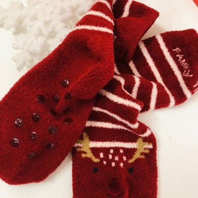 Meias vermelhas felpudas com motivos de rena, riscas brancas e pontos antiderrapantes ao lado de um floco de neve decorativo branco
