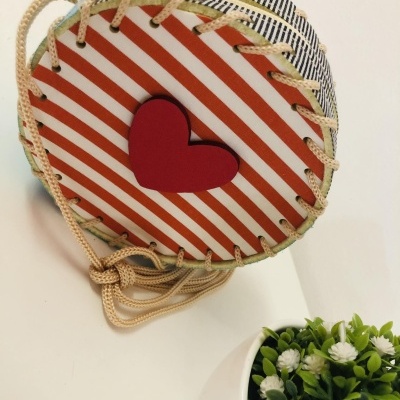 Saco redondo riscado com coração vermelho e cordão ao lado de vaso com plantas