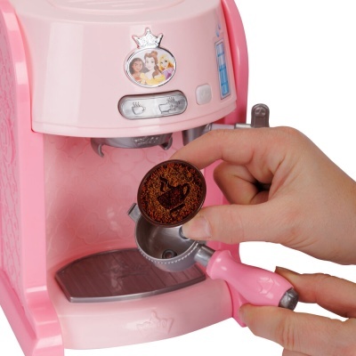 Máquina de café de brinquedo rosa com adesivo de princesas e mãos segurando acessórios