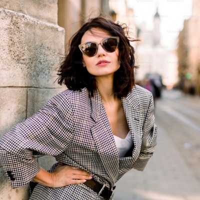 Mulher com casaco xadrez preto e branco e óculos de sol dourados numa rua urbana