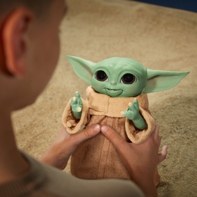 Boneco de Baby Yoda a ser segurado por uma pessoa com fundo bege