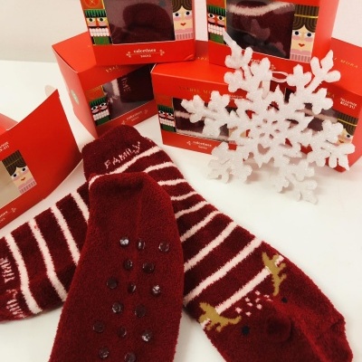 Meias térmicas bordô com riscas brancas e padrão de rena, caixas vermelhas VÄRME MORA ao fundo.