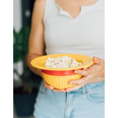 Chapéu amarelo com pipocas segurado por pessoa em ambiente interior