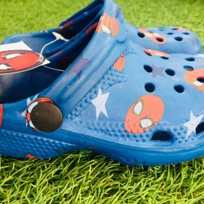 Clogs azuis com estampas do Spiderman sobre relva artificial verde