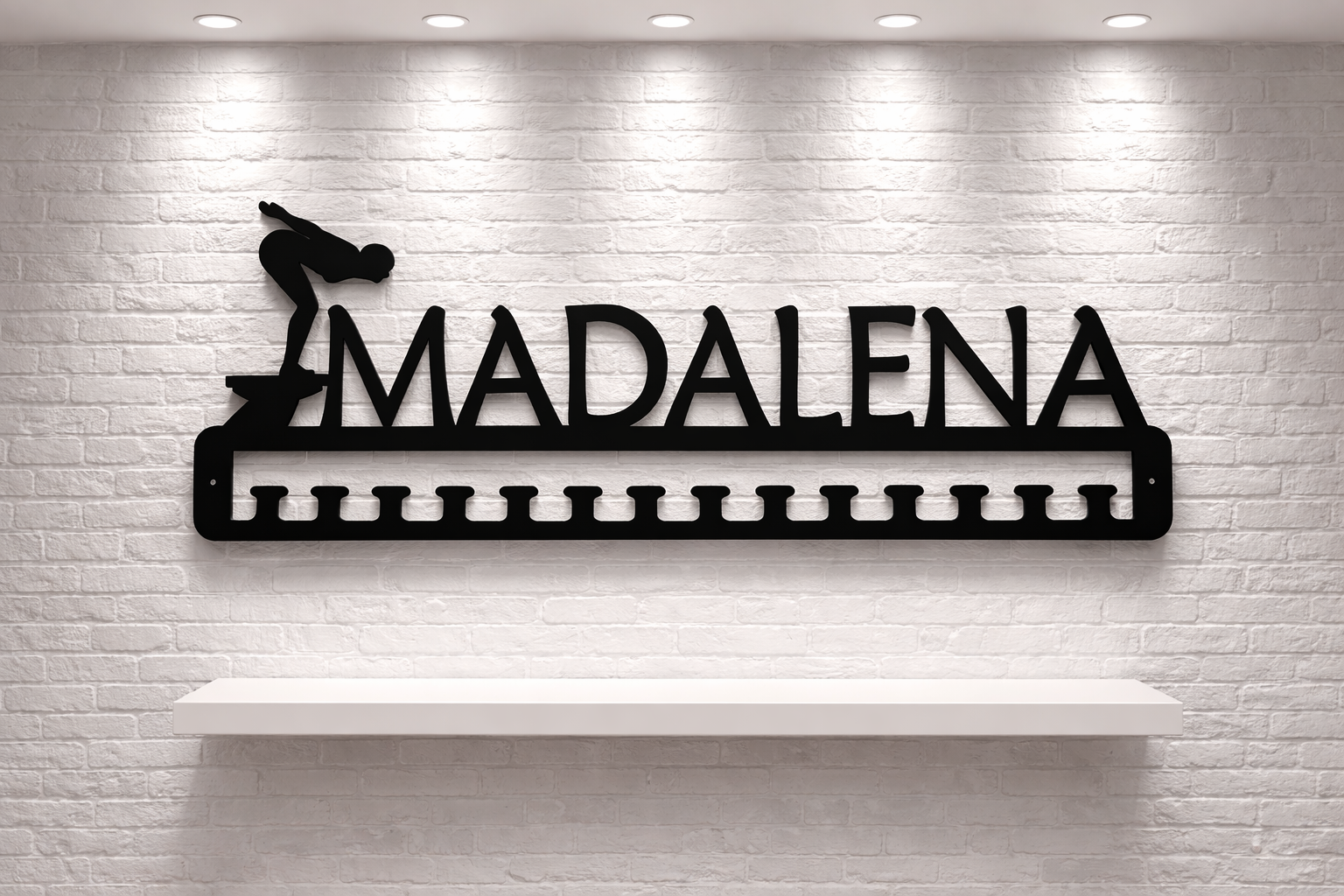 Cabide de ferro preto com nome Madalena e figura de mergulhador montado em parede branca.