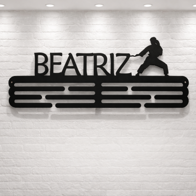 Suporte de parede em metal preto com nome BEATRIZ e figura de artes marciais na parede de tijolo branco.