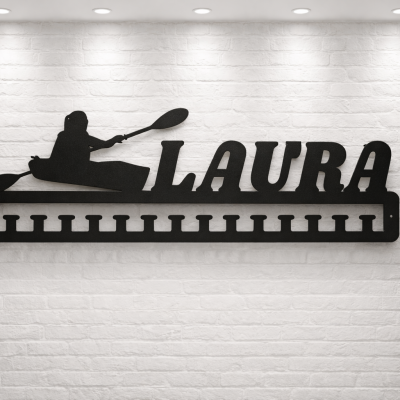 Placa decorativa preta de metal com a palavra LAURA e figura de caiaque numa parede branca