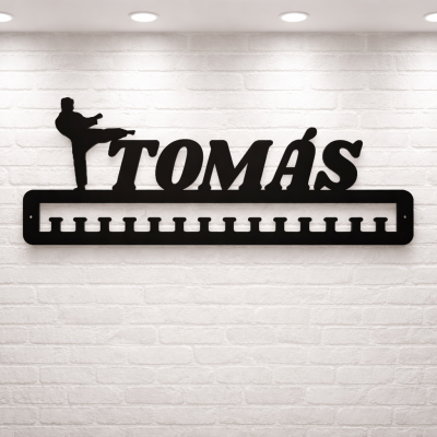 Suporte de parede preto com ganchos e texto TOMÁS em parede de tijolos