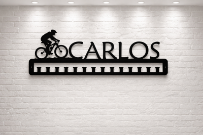 Prateleira metálica preta com ciclista e nome CARLOS numa parede branca de tijolos