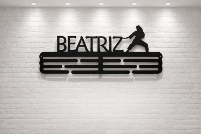 Suporte de parede em metal preto com nome BEATRIZ e figura de artes marciais na parede de tijolo branco.