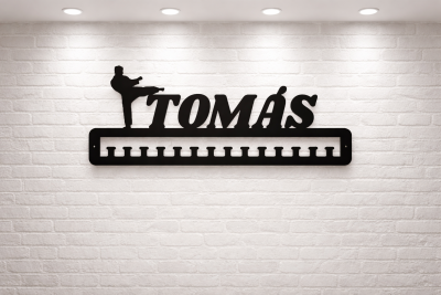 Suporte de parede preto com ganchos e texto TOMÁS em parede de tijolos