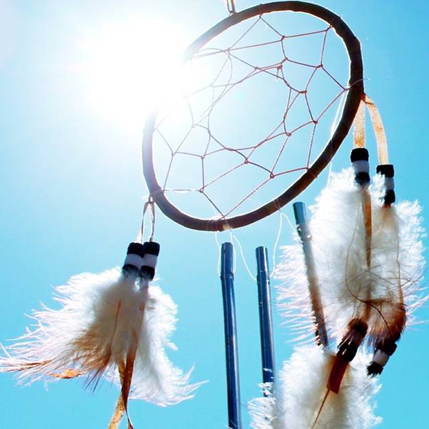 Apanhador de sonhos com penas brancas penduradas contra céu azul e sol