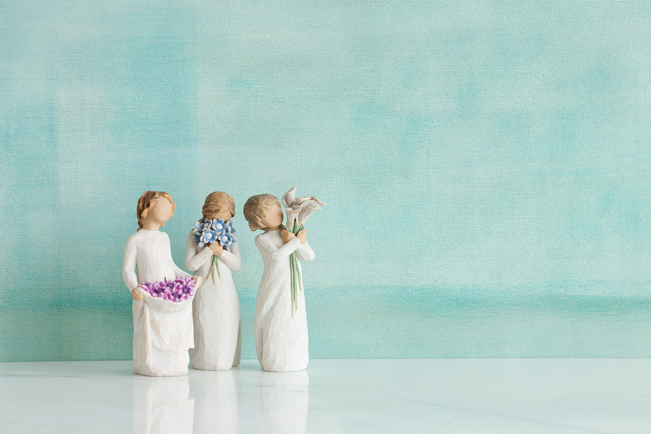 Três figuras femininas decorativas em resina segurando flores de cores variadas