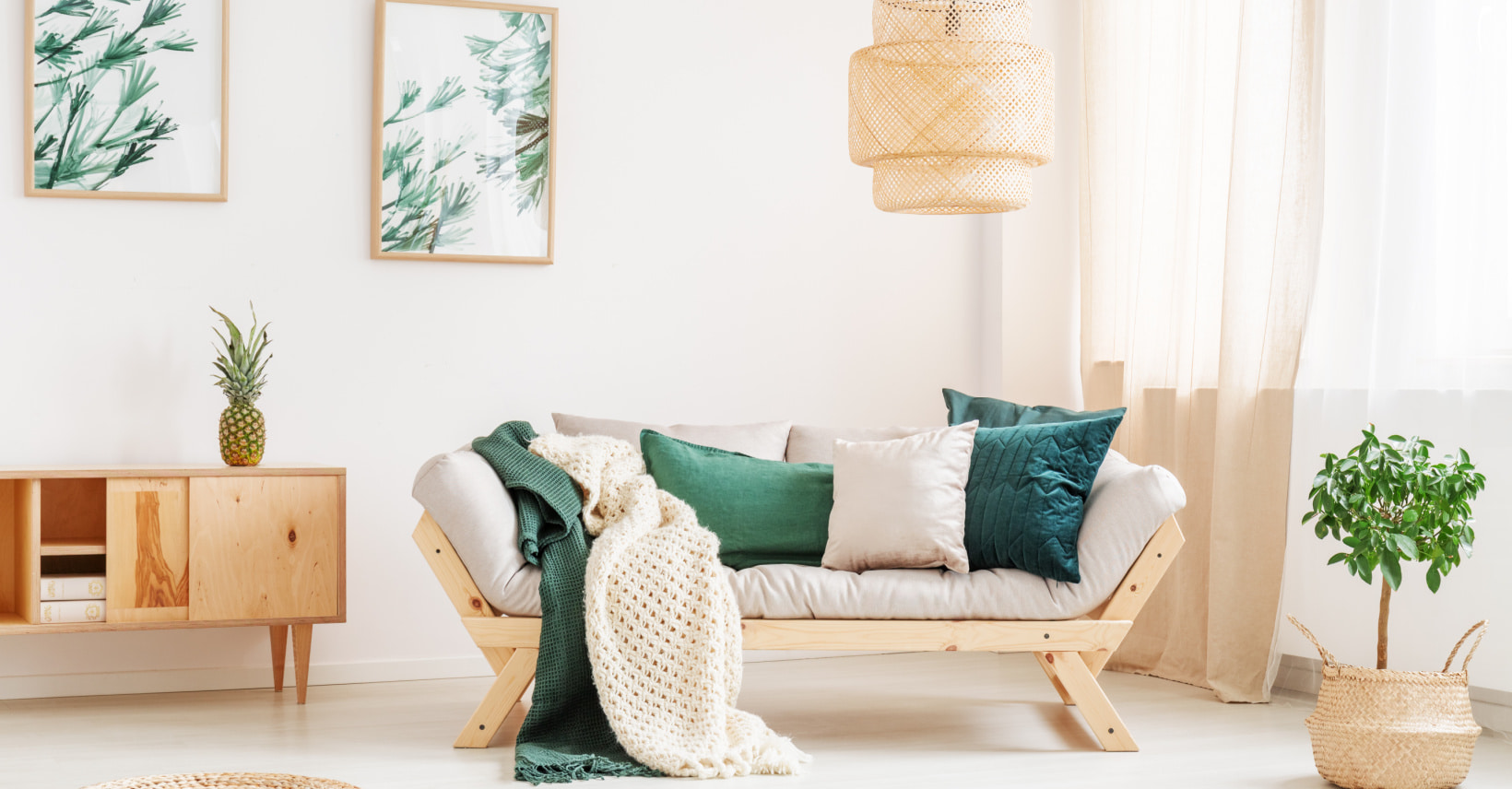 Sala de estar com sofá de madeira e almofadas verdes, quadros de folhas e plantas