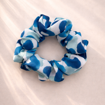 Scrunchie azul com padrão leopardo em fundo branco.