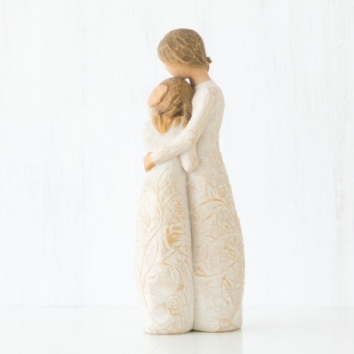 Escultura decorativa de duas figuras femininas abraçadas em material cerâmico com padrões florais.