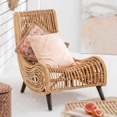 Cadeira de rattan com almofadas rosas numa sala clara e decorada.