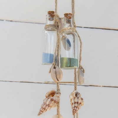 Frascos de vidro com areia colorida e conchas penduradas em corda