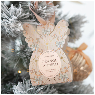 Embalagem em forma de anjo creme com texto e padrão floral pendurada em árvore de Natal com neve artificial