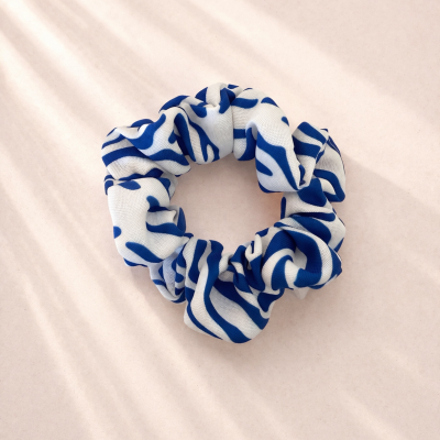 Elástico de cabelo scrunchie branco com padrão azul sobre fundo bege