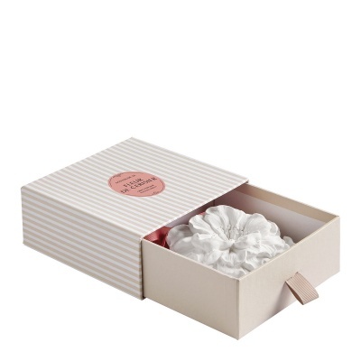 Caixa bege com riscas brancas e flor decorativa branca