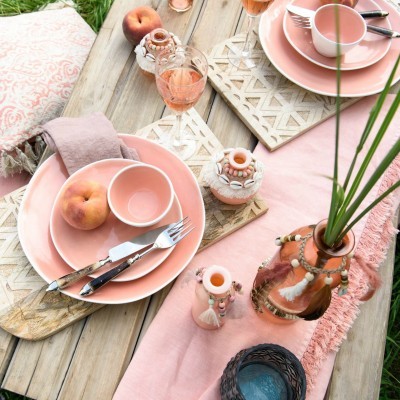 Mesa de madeira ao ar livre com pratos e tigelas cor-de-rosa, talheres, jarros decorativos e frutas