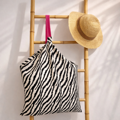 Saco com padrão de riscas preta e branca pendurado numa escada de madeira com chapéu de palha ao lado.
