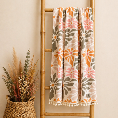 Cobertor floral com pompons pendurado em escada de bambu ao lado de cesto com plantas secas