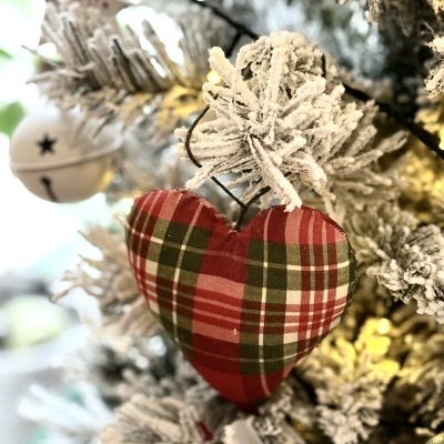 Ornamento de coração xadrez vermelho e verde numa árvore de Natal com efeito de neve