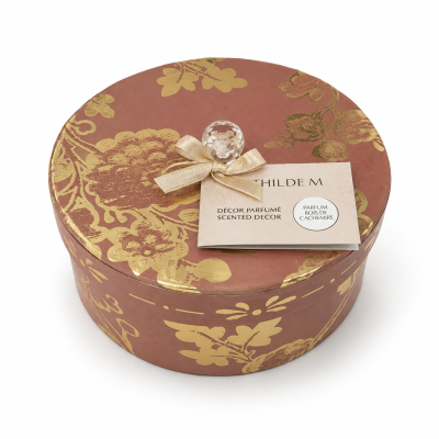 Caixa redonda decorativa castanho-avermelhada com padrão floral dourado e etiqueta branca