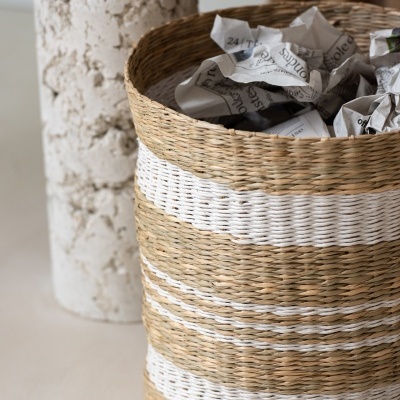 Cesto redondo em fibras naturais bege e branco com jornais amassados.