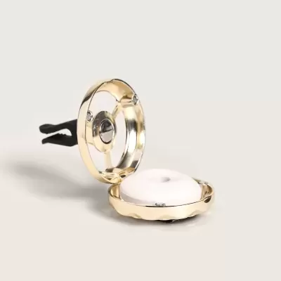 Clip dourado redondo com objeto branco interior sobre fundo cinzento claro