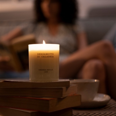 Vela branca acesa com etiqueta e livros empilhados ao fundo