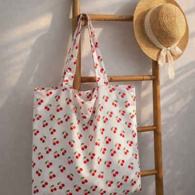 Bolsa de pano com padrão de cerejas e chapéu de palha pendurados numa estrutura de madeira