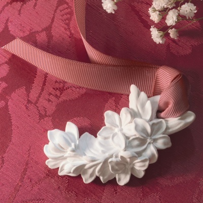 Flores brancas decorativas em cerâmica com fita rosa sobre tecido vermelho texturado e pequenas flores brancas