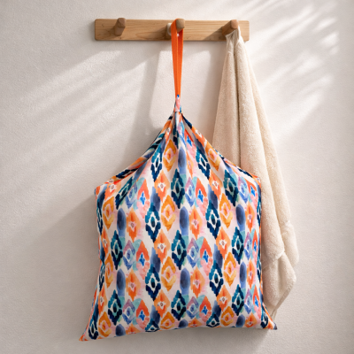 Saco de tecido colorido e toalha pendurados num cabide de parede de madeira.