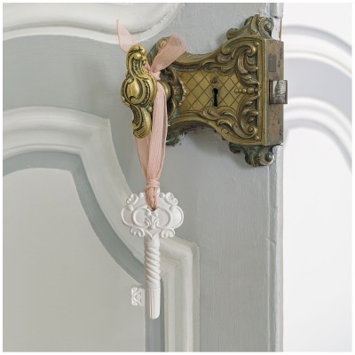 Fechadura antiga dourada com chave decorativa branca pendurada numa porta branca