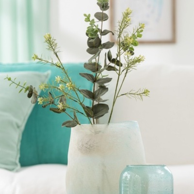 Arranjo floral em vaso branco fosco com castiçal azul e vela verde na sala