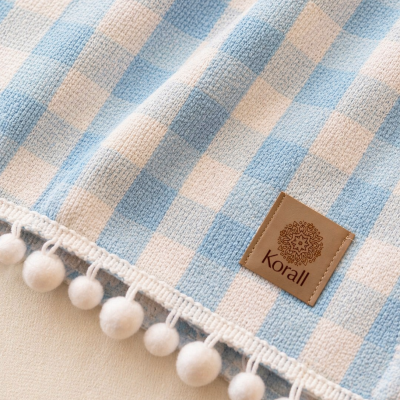 Pano azul e branco xadrez tricotado com pompons brancos na borda e etiqueta Korall.