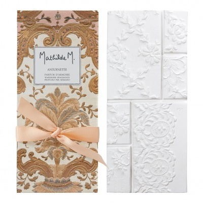 Embalaagem de perfume com padrão barroco, laço rosa e placa branca com relevo floral