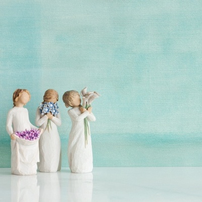 Três figuras femininas decorativas em resina segurando flores de cores variadas