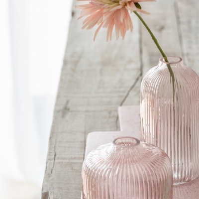 Vasos de vidro rosado estriados com flor cor-de-rosa e superfície de madeira clara