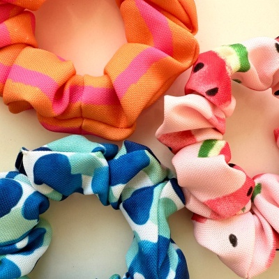 Três scrunchies coloridos com diferentes padrões sobre fundo bege