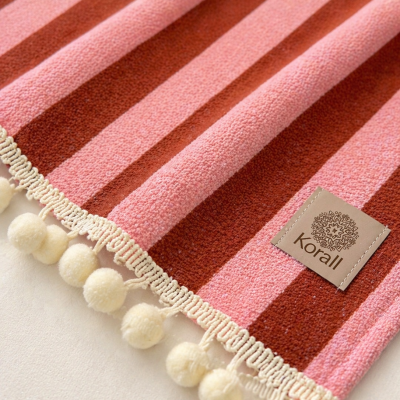 Toalha rosa e vermelha com pompons e etiqueta Korall