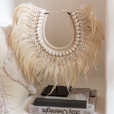 Colar decorativo de penas brancas e bege com contas num nicho branco