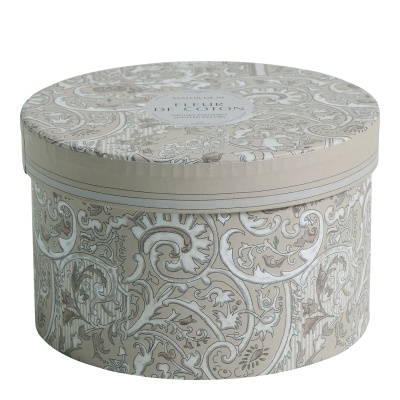 Caixa redonda decorativa bege com padrão floral e arabescos e etiqueta no centro da tampa