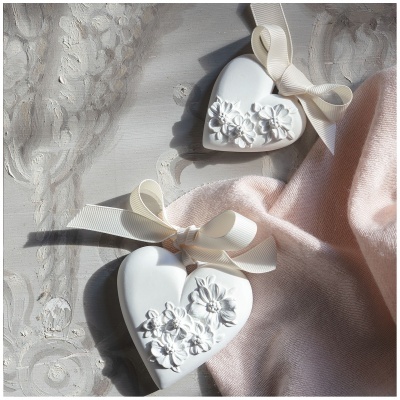 Duas decorações de coração brancas com flores em relevo sobre superfície cinza e tecido rosa claro